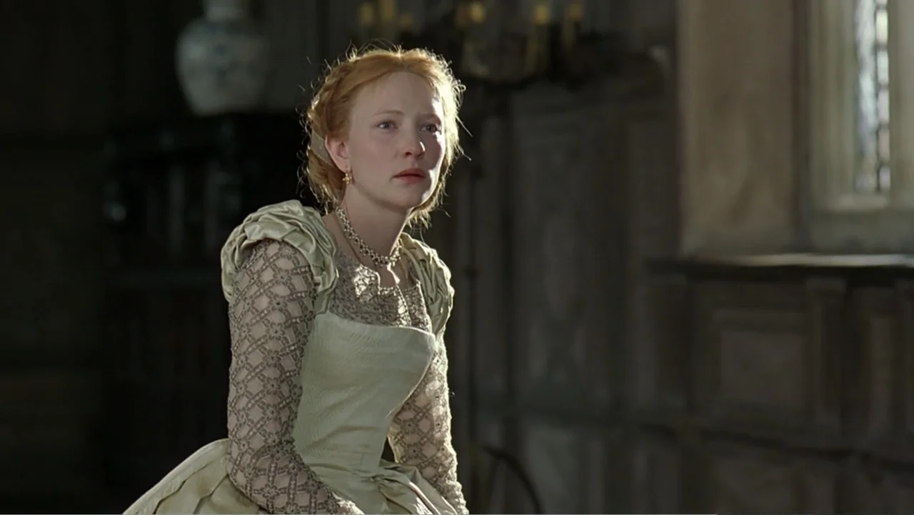 Elizabeth (1998) movie still: medium — A dark, wood-paneled room is lit by light filtering through a window. A woman wearing an intricate period…