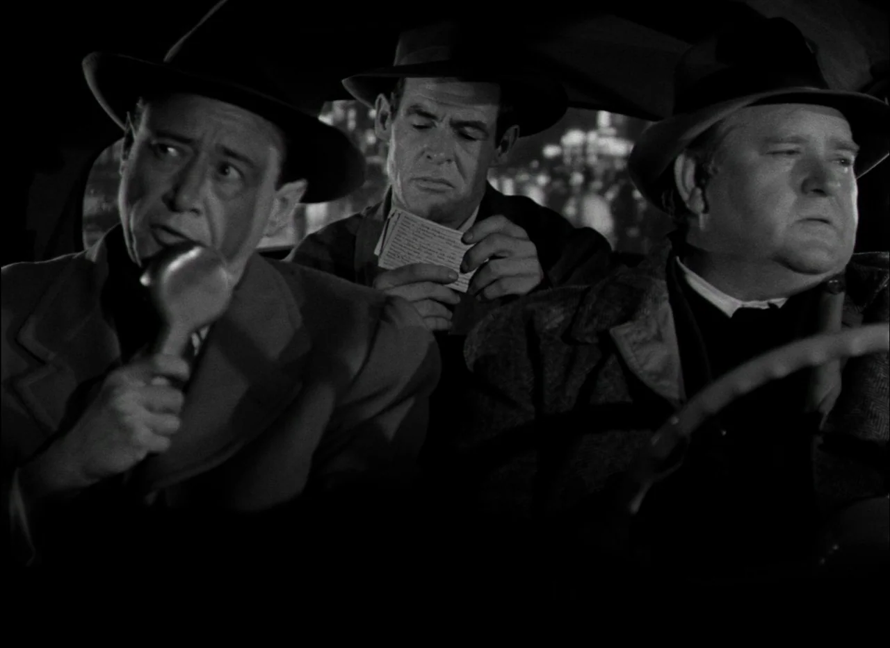 On Dangerous Ground (1951) movie still: medium — Three men in fedoras and overcoats sit together inside the dark interior of a car. The man on the…