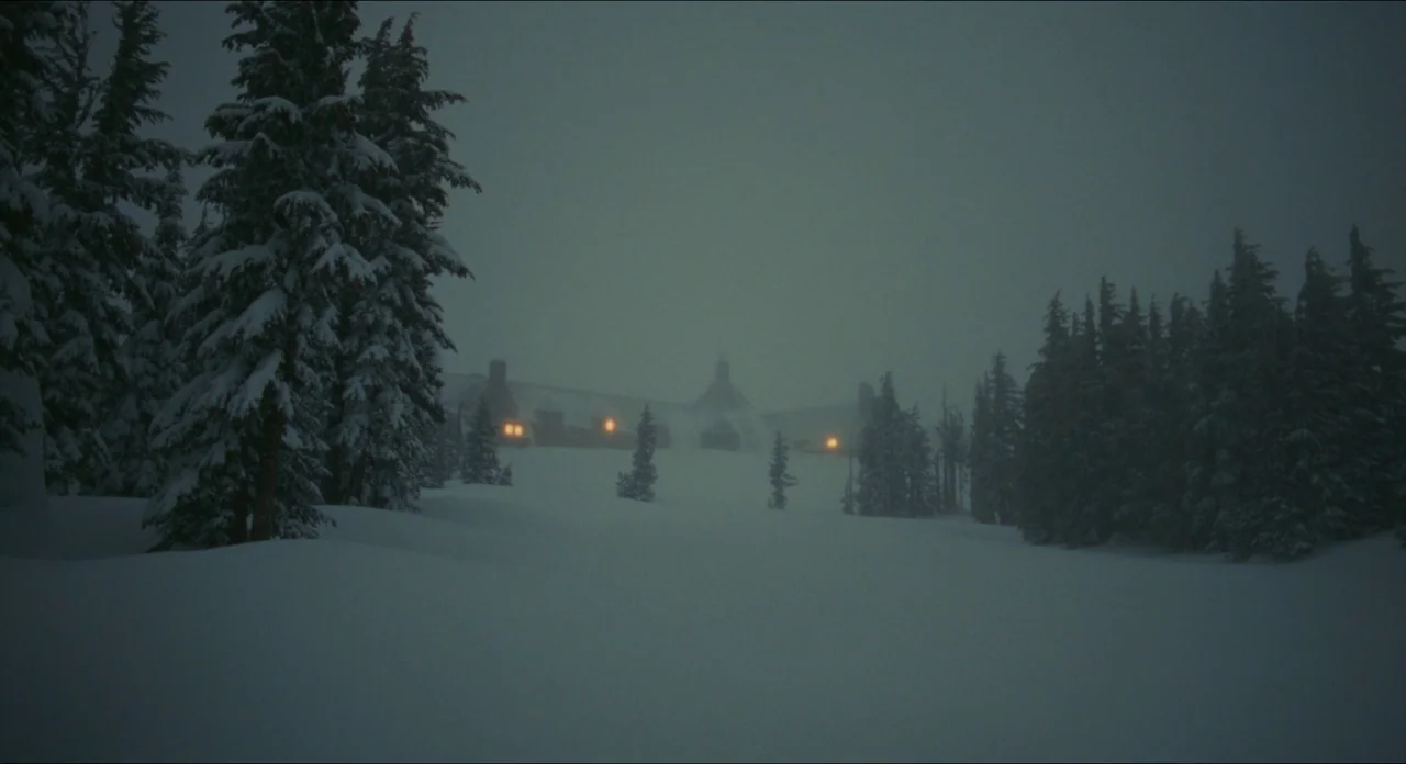 Doctor Sleep movie still: establishing — A large stone hotel building sits on a snowy ridge during a dark storm. Coniferous trees covered in snow…