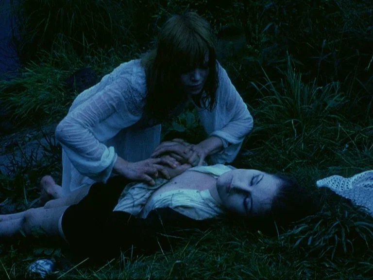Der Bomberpilot (1970) movie still: medium — Two women are positioned on dark, damp-looking grass in a field at night. One woman kneels over the…