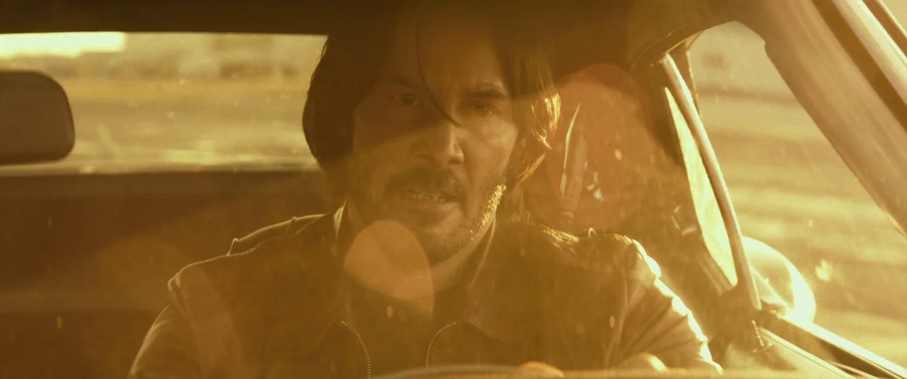 John Wick (2014) movie still: closeup — A man drives a vintage car during the golden hour sunset. Bright lens flares obscure parts of the windshield.