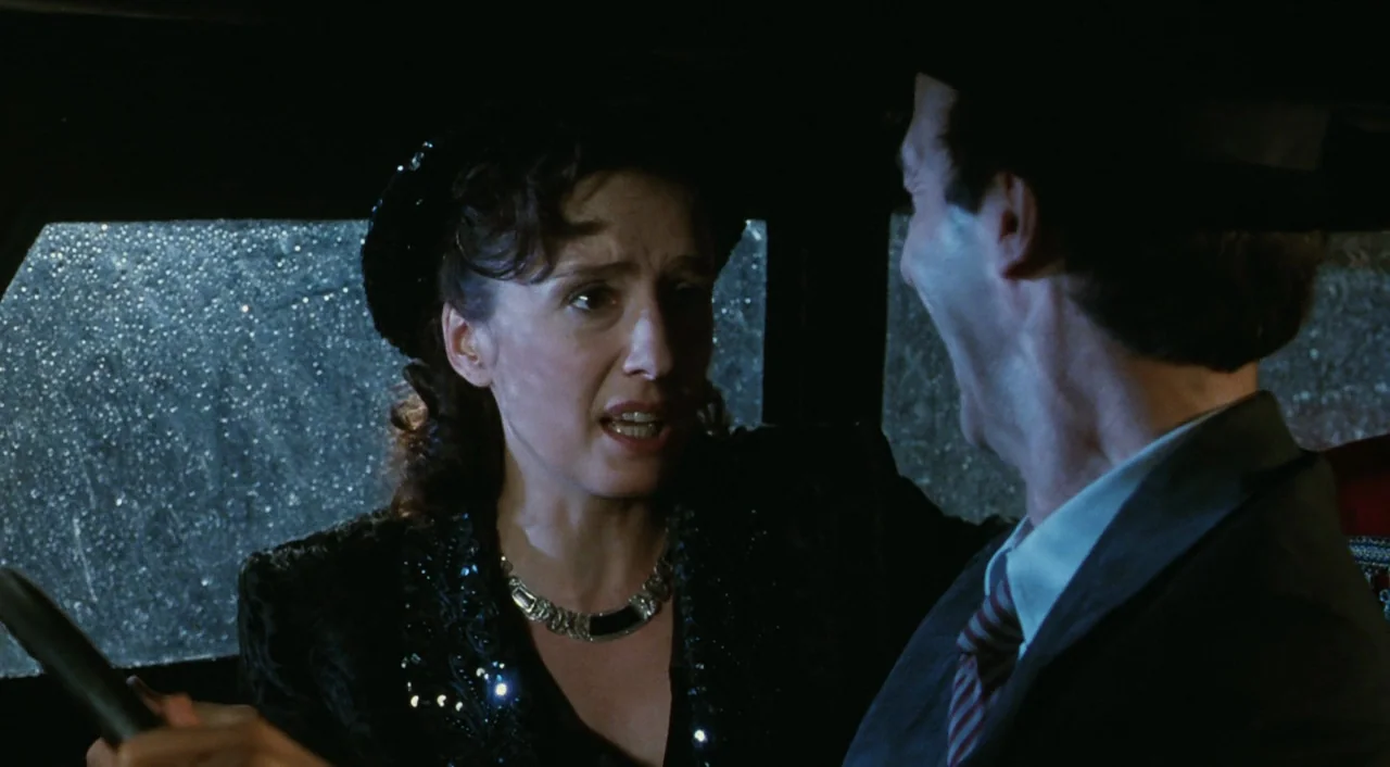 Life is Beautiful (1997) movie still: medium — Two people are conversing inside a vehicle during a dark, rainy night. Rainwater streaks across the…