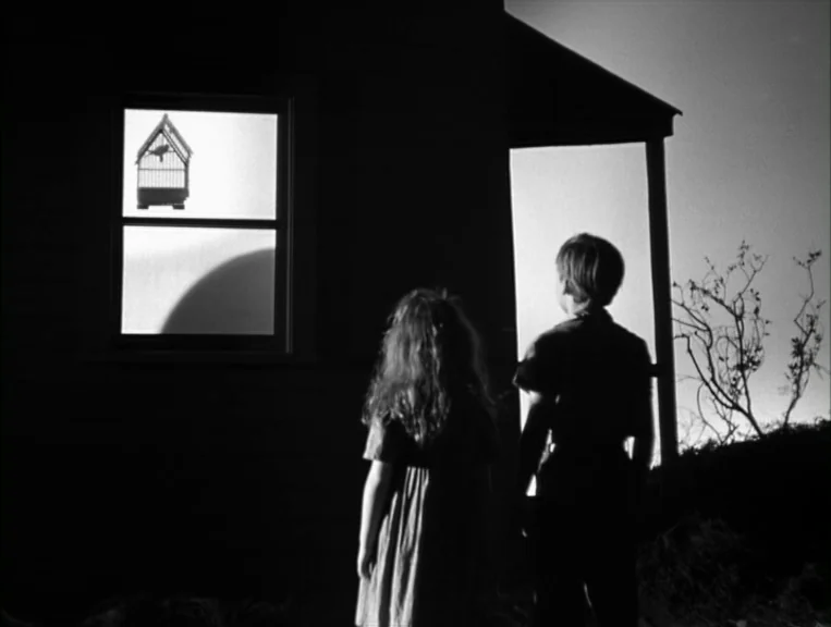 The Night Of The Hunter (1955) movie still: medium — A dark, silhouetted house exterior features a glowing window showcasing a hanging birdcage. Two…