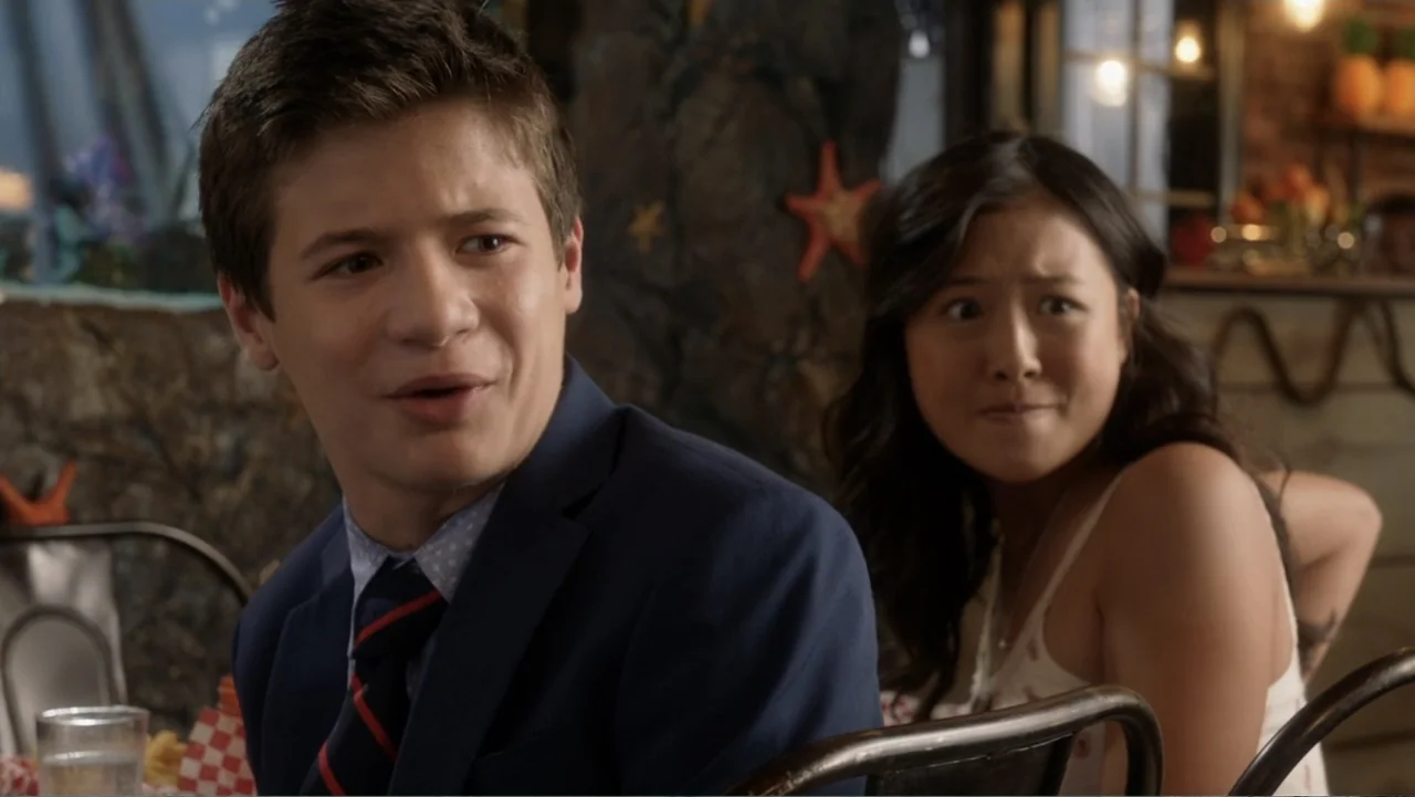 Rufus 2 (2017) movie still: medium — A casual dining venue with a textured stone wall decorated with starfish and decor. A teenage boy in a blazer…