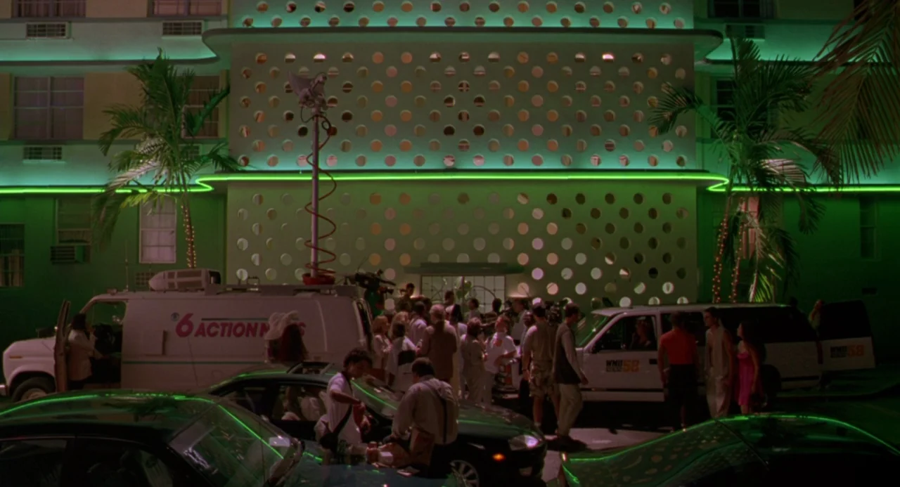 The Birdcage (1996) movie still: wide — A modernist building at night features a repeating circular pattern on its facade. A crowd of people stand…