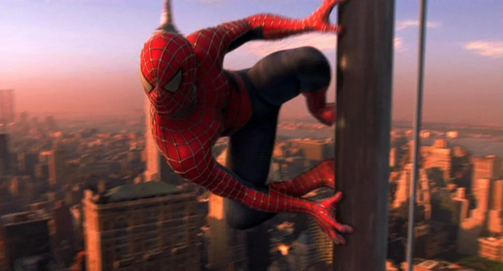 Spider-Man (2002) movie still: medium — A man in a red and blue spider costume clings to a steel beam. The New York city skyline stretches out below…