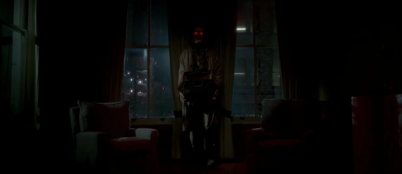 Gerald’s Game (2017) movie still: fullbody — A dark hotel room interior at night is illuminated by light from a window. A tall, thin man stands…