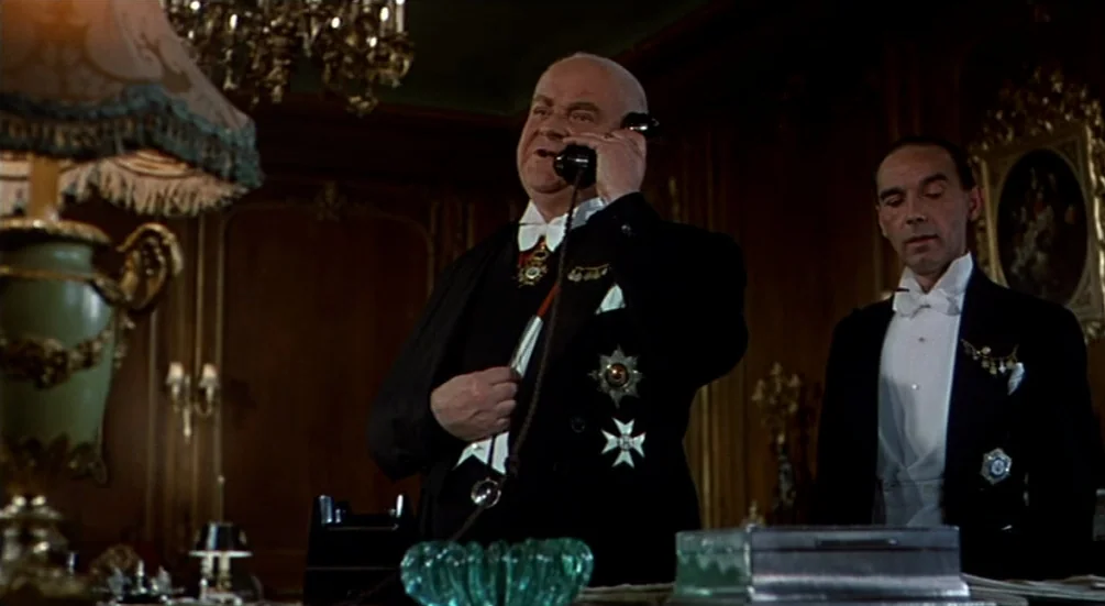 The Man Who Knew Too Much (1956) movie still: medium — A richly decorated wood-paneled room features period furniture and antique decorative…