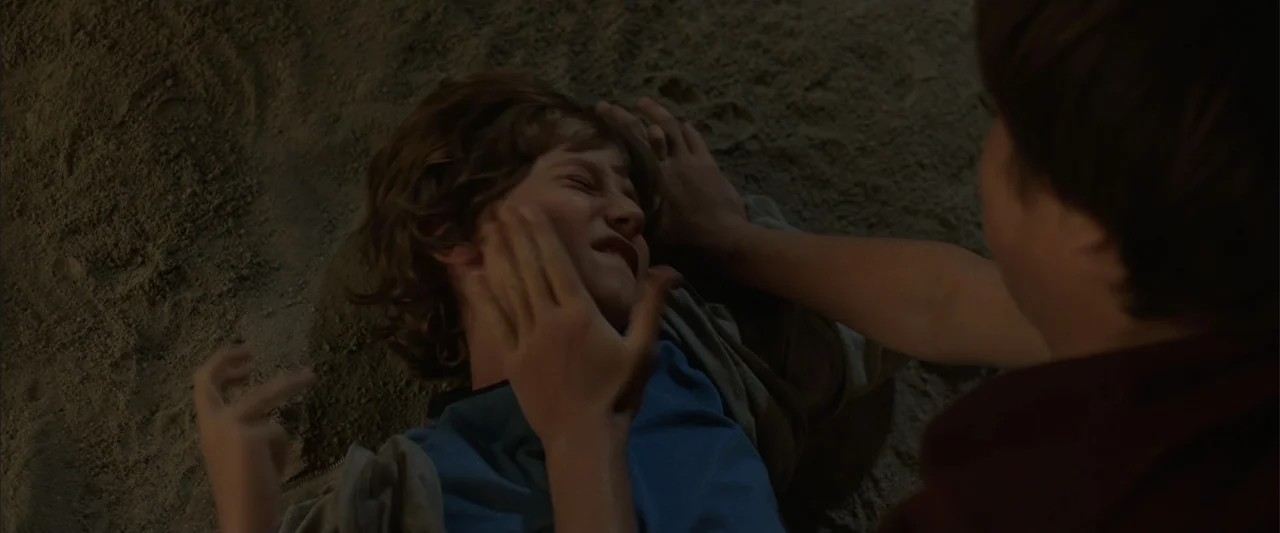 Vacation (2015) movie still: medium — A sandy ground surface serves as the setting for a physical struggle. One child lying down is being struck in…