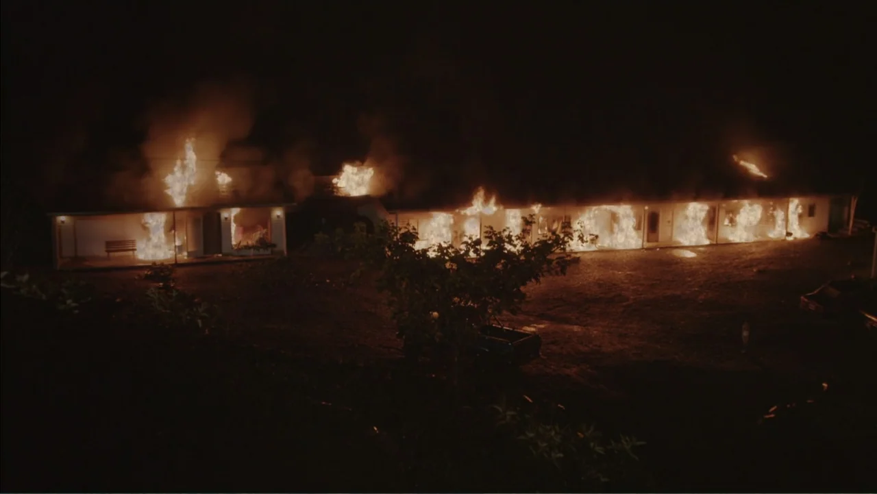 Boy (2010) movie still: wide — A long, single-story motel building is engulfed in flames at night. Bright fire burns through several doorways and…