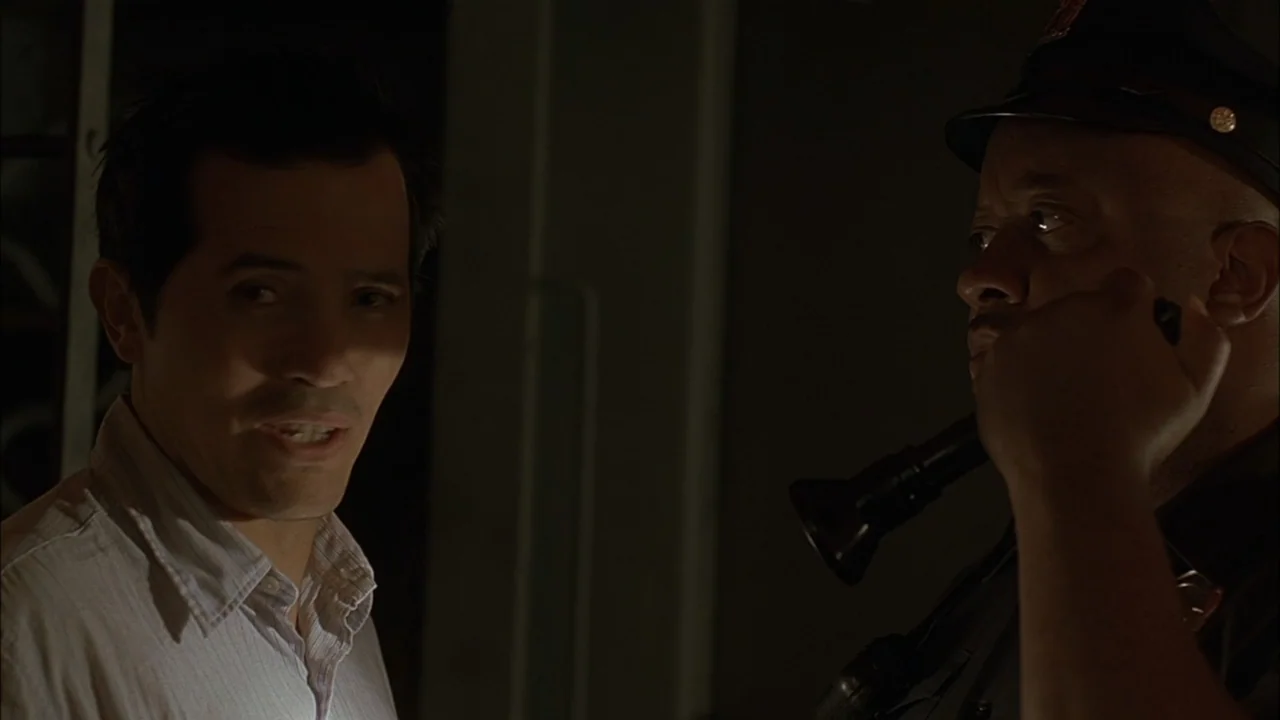 The Babysitters (2008) movie still: medium — A dimly lit interior space features two men standing close to each other. One man speaks toward a…