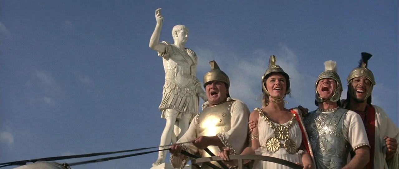 History of the World: Part 1 (1981) movie still: medium — A group of four actors in Roman-style armor and tunics stand together in a chariot. A…