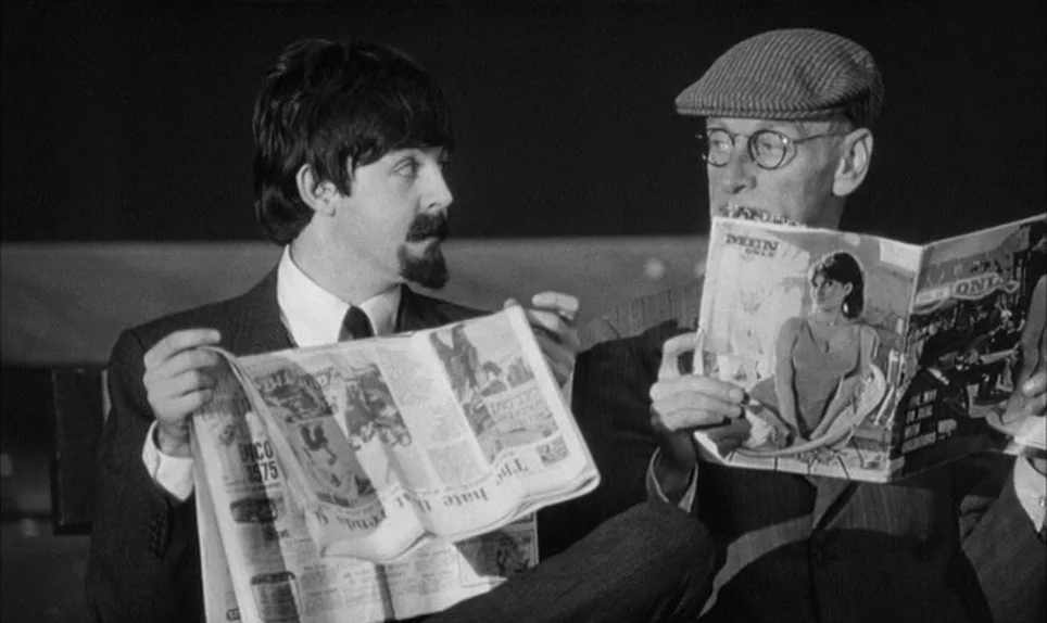 A Hard Days Night (1964) movie still: medium — Two men sit together reading in what appears to be a train carriage interior. One man holds a…