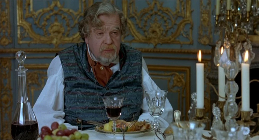 The Last Mistress (2007) movie still: medium — A man sits at an ornate table in a room with elaborate gold-trimmed wall moldings. He is eating a…