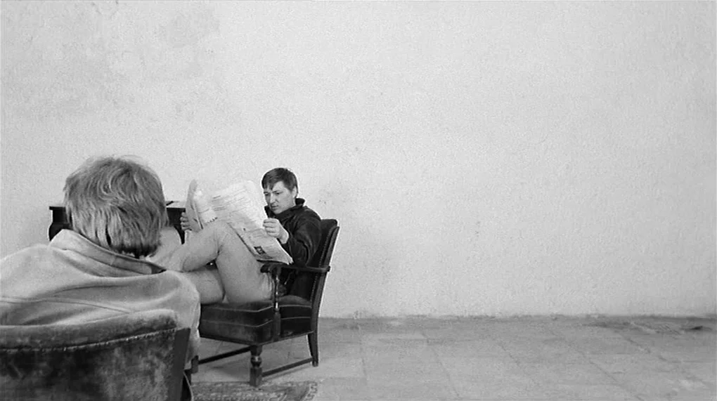 Love Is Colder Than Death (1969) movie still: wide — A sparse, minimalist room features plain white walls and a stone tile floor. Two men sit in…