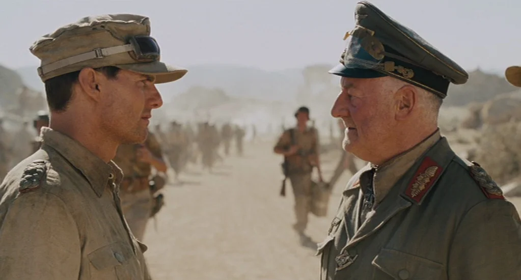 Valkyrie (2008) movie still: medium — A dusty desert landscape filled with hazy light serves as the background for soldiers. Two officers in tan…