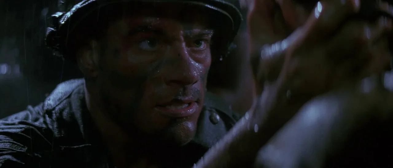 Universal Soldier (1992) movie still: closeup — A soldier wearing a helmet is out in the rain at night. He is locked in a close-up interaction with…