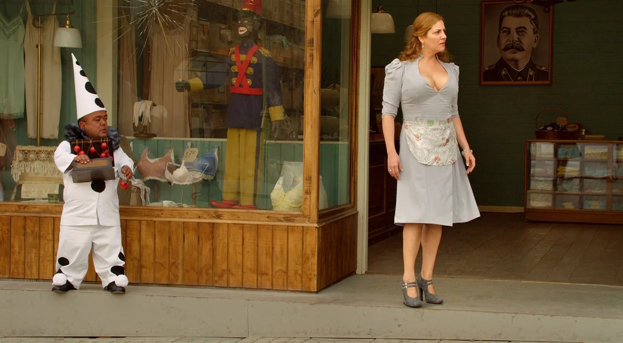 Dance of Reality (2013) movie still: fullbody — A wooden store facade features a display window with lingerie and a nutcracker figurine. A woman…