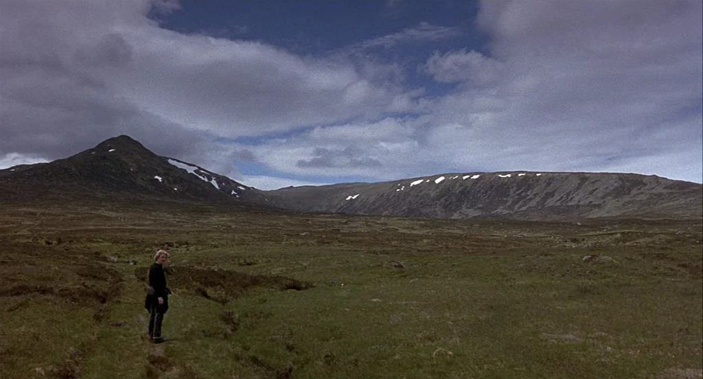 Trainspotting (1996) movie still: wide — A vast, expansive moorland valley is surrounded by rolling mountains with patches of snow. A solitary young…