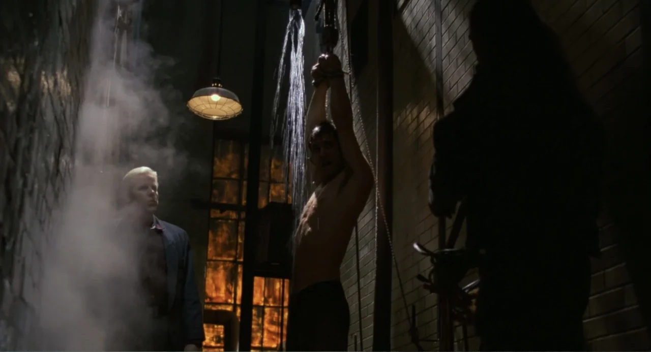 Lethal Weapon (1987) movie still: medium — A dark industrial basement features brick walls and a large glowing furnace background. A shirtless man…