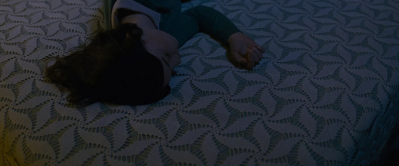 Stoker (2013) movie still: closeup — A dark, dimly lit room contains a bed covered by a patterned white lace spread. A person with dark hair lies…