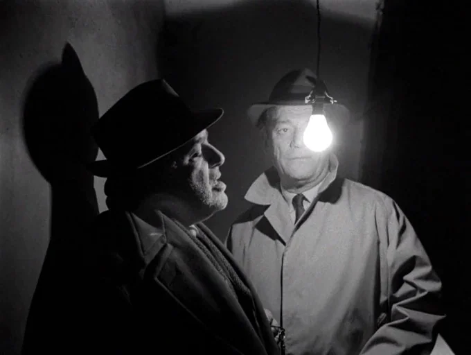 Alphaville (1965) movie still: medium — A dimly lit room features a single hanging lightbulb casting a sharp shadow. Two men in fedoras and…