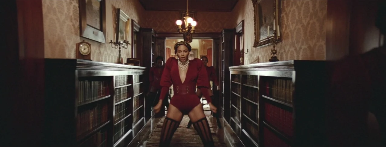 Lemonade (2016) movie still: fullbody — A symmetrical room lined with dark wood bookshelves and antique patterned wallpaper. A woman in a burgundy…