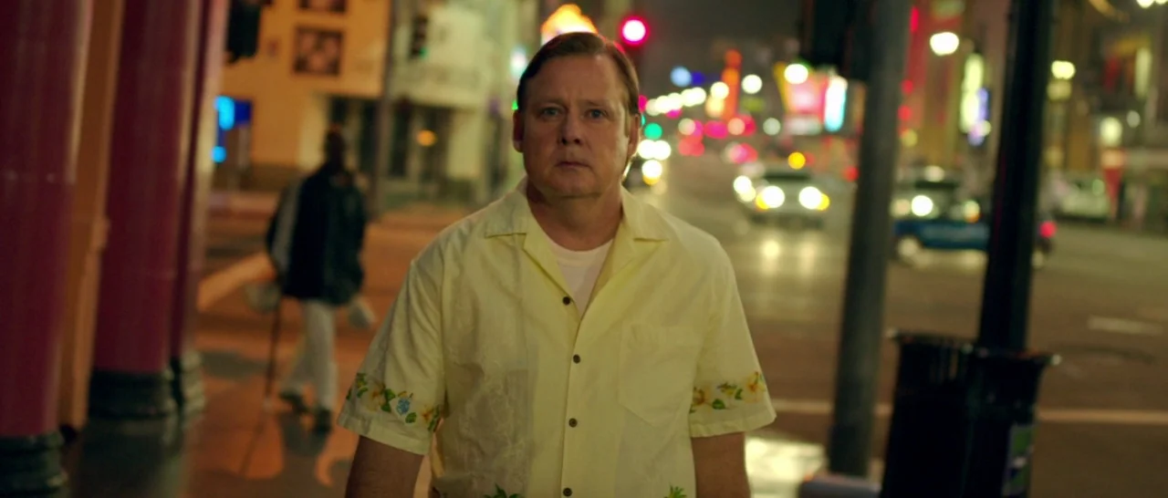 God Bless America (2011) movie still: medium — A man in a floral shirt walks toward the camera on a city sidewalk. The background is a blurred night…