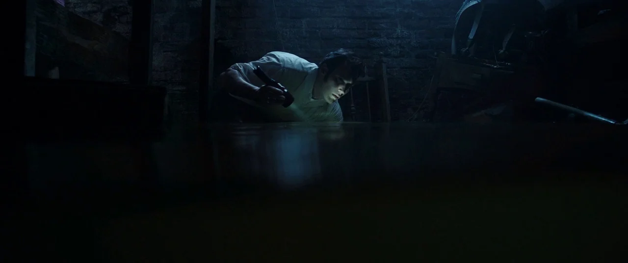 The Conjuring 2 (2016) movie still: medium — A dark subterranean space features rough brick walls and wooden structural elements. A man lies on the…