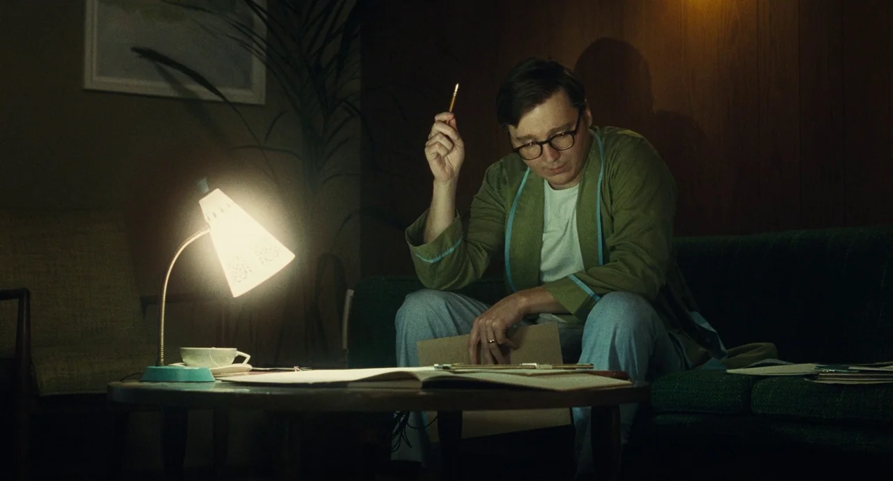 The Fabelmans (2022) movie still: medium — A dark, wood-paneled living room features a green couch and a mid-century coffee table. A man in a…
