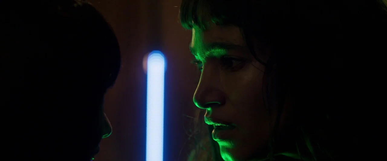 Prisoners of the Ghostland (2021) movie still: closeup — A dark space features a woman in profile illuminated by a sharp green light source. A…