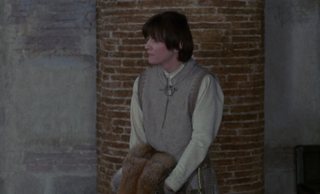 Blanche (1971) movie still: medium — A stone interior features a curved red brick column against a textured wall. A young man wearing a wool vest…