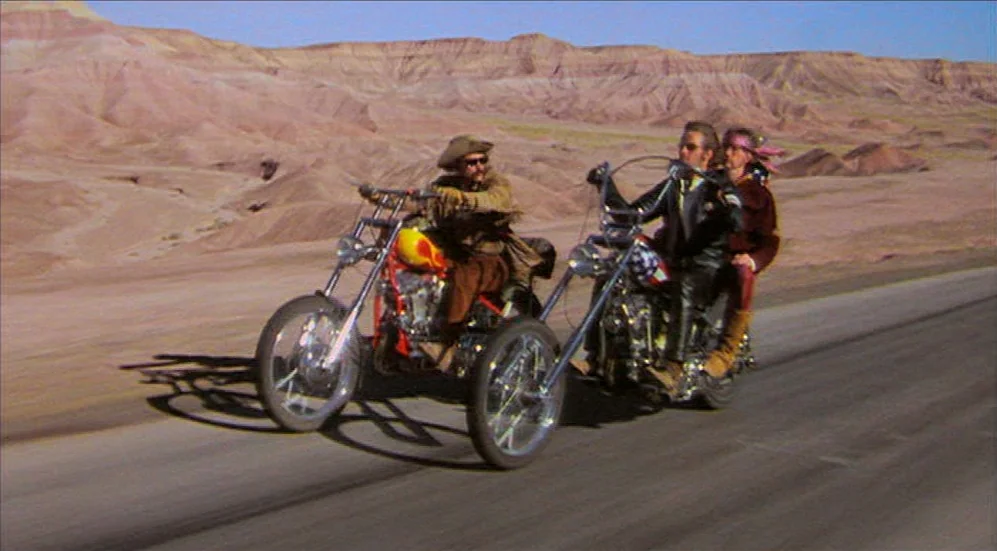 Easy Rider (1969) movie still: wide — A desolate desert highway stretches across a vast landscape of red-brown arid hills. Two custom chopper…