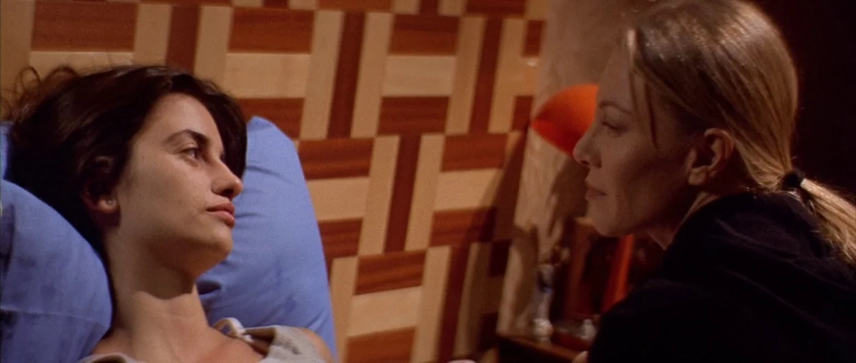 All About My Mother (1999) movie still: medium — A bedroom features a wall with a prominent brown and white geometric pattern. A woman lies on a…
