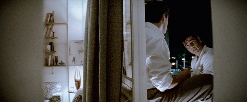 Che Part 1 (The Argentine) (2008) movie still: medium — A mid-century modern hotel room interior with a bookshelf and a stylized table lamp. Two men…