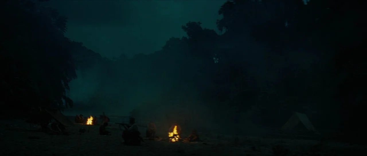 The Lost City of Z (2016) movie still: wide — A dark riverbank at night features several small fires burning among scattered groups of people.…