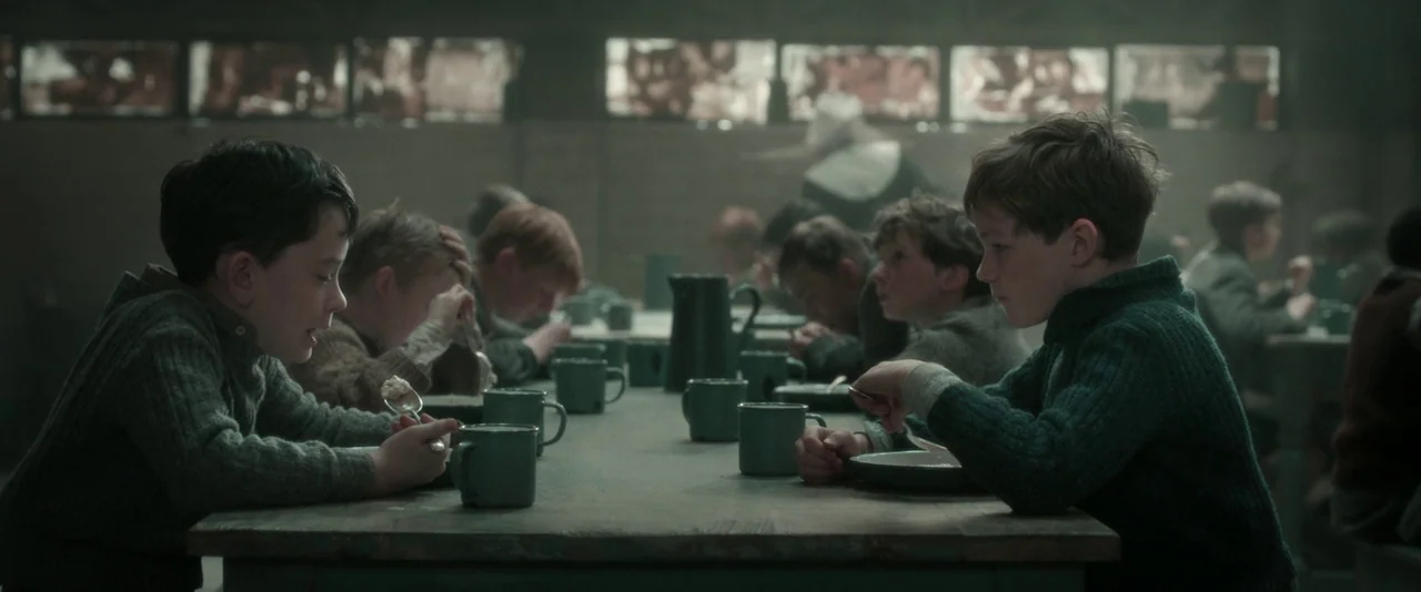 Pan (2015) movie still: medium — A long, dimly lit dining hall filled with rows of boys eating at long tables. Young boys in matching knit sweaters…