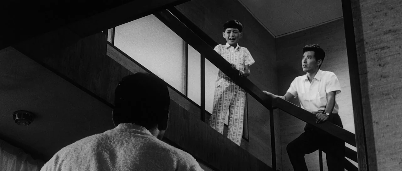 High and Low (1963) movie still: medium — A dark, modern interior staircase landing with clean lines and wood-paneled walls. A man and a young boy…