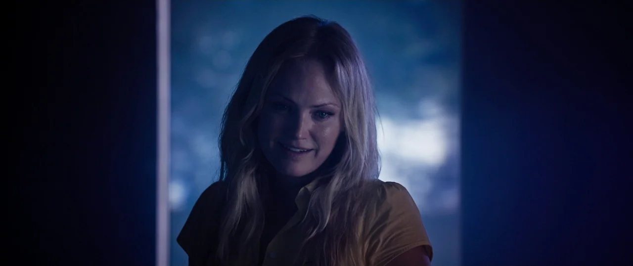 Final Girls (2015) movie still: medium — A dark indoor space is lit by a large window casting deep blue light. A woman with blonde hair stands in…