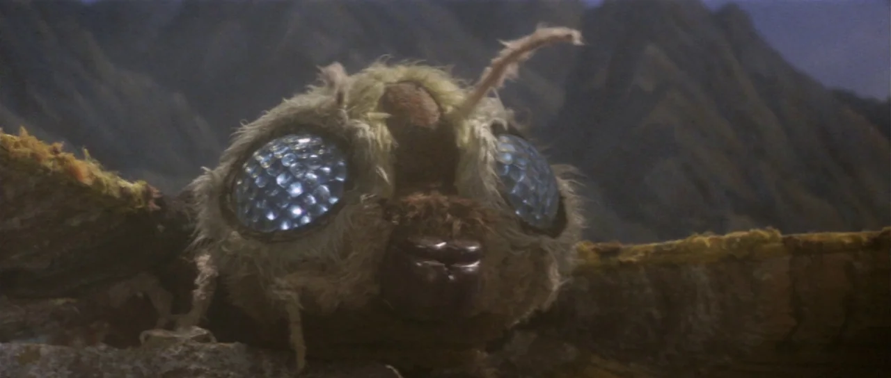 Ebirah Horror of the Deep (1966) movie still: closeup — A furry moth puppet sits on a rocky ridge in front of mountain peaks. The creature stares…