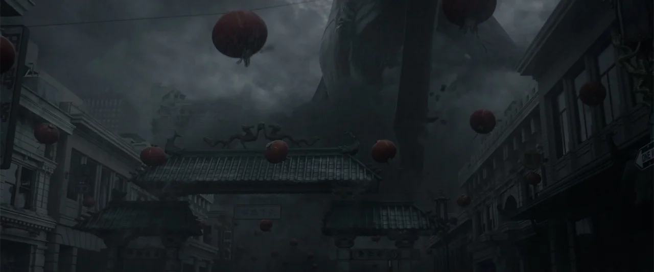 Godzilla (2014) movie still: wide — A dark, rainy chinatown street features an ornate stone gate adorned with traditional carvings. Red lanterns…