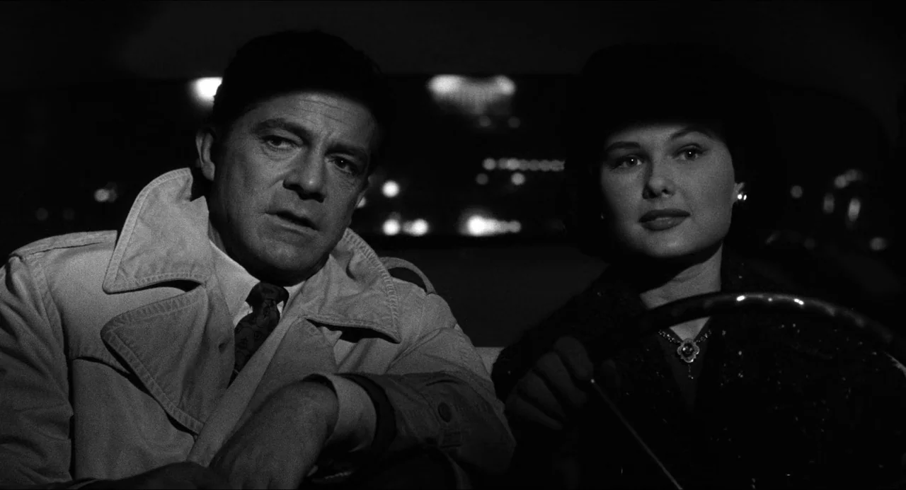 The Fearmakers (1958) movie still: medium — A man and woman are seated inside a dark vehicle at night. Out-of-focus city lights are visible through…