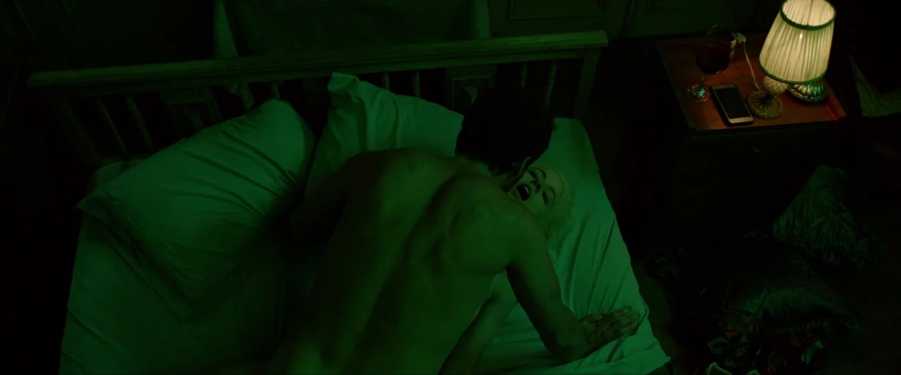 Ema (2019) movie still: medium — A dimly lit room at night features a wooden bed frame with white linens. A man and a woman are positioned together…