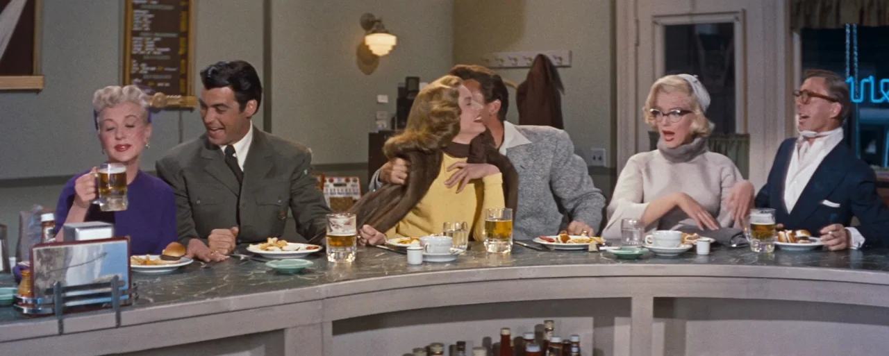How to Marry a Millionaire movie still: wide — A curved diner counter with three couples sitting and socializing over drinks. The walls are light…