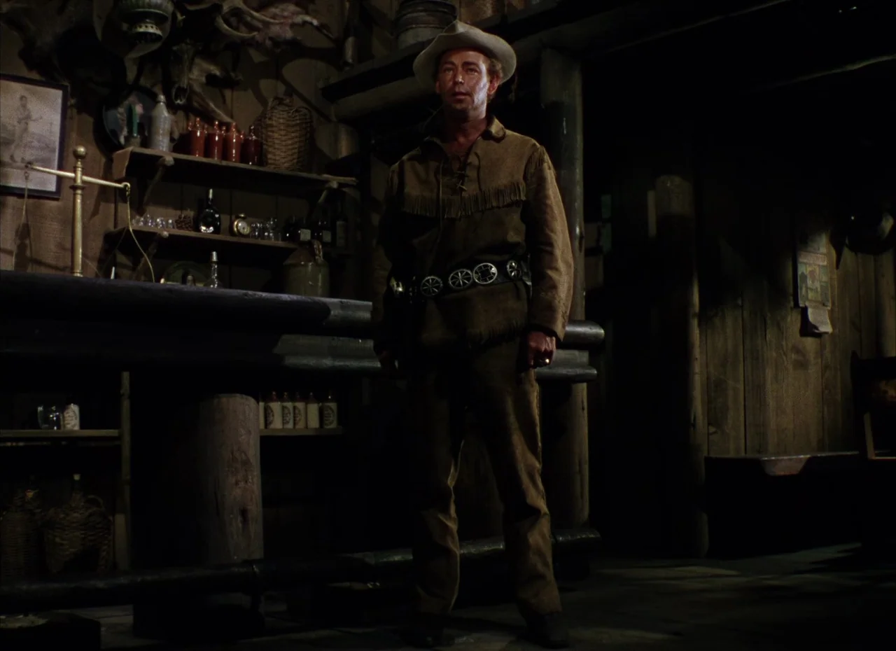 Shane (1953) movie still: fullbody — A rustic wooden room contains shelves filled with bottles, a scale, and taxidermy mounts. A man wearing western…