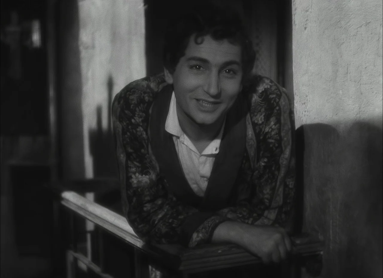 Les Enfants Du Paradis (1945) movie still: medium — A man stands on a shadowed balcony with textured plaster walls visible behind him. The man leans…