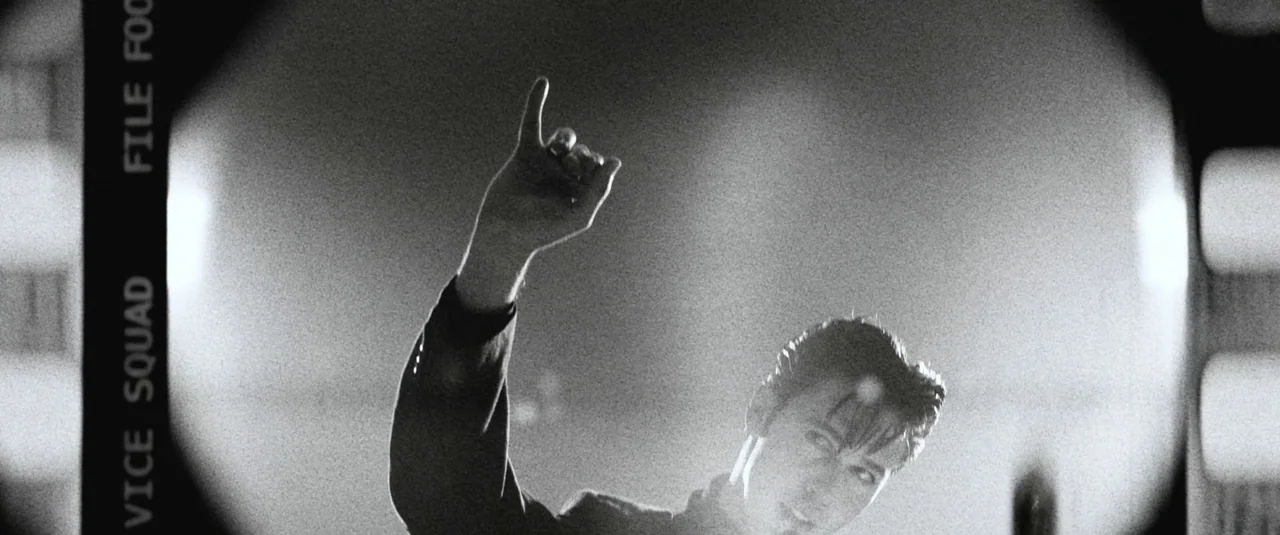 Elvis (2022) movie still: medium — A person stands under a dramatic spotlight on a dark performance platform. The figure reaches an arm toward the…