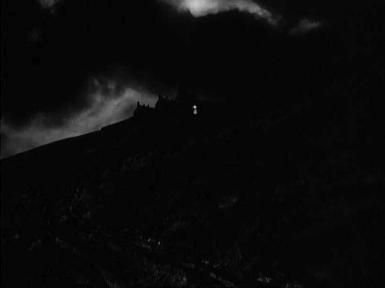 Oliver Twist (1948) movie still: establishing — A dark, silhouetted building sits on a steep, barren hillside under stormy clouds. A single point of…