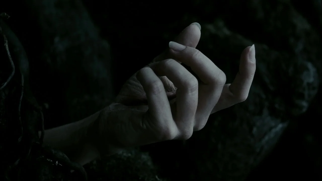 Sleepy Hollow (1999) movie still: closeup — A pale, human hand reaches out from within a cluster of dark tree roots. The hand is positioned against…