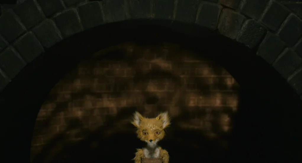 Fantastic Mr. Fox (2009) movie still: medium — A small fox character stands centered before a large, dark circular brick archway. The scene is dimly…